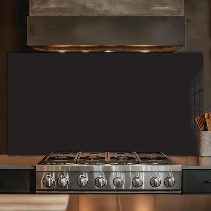 Black tempered glass kitchen backsplash behind modern gas stove with dark range hood